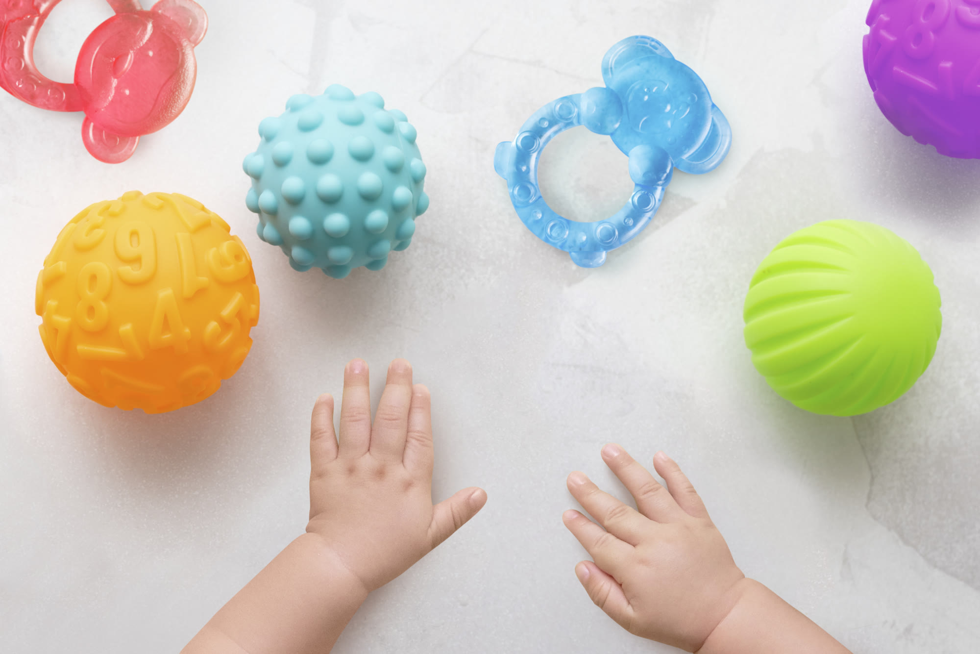 A baby’s hands reaching for colorful sensory balls and teethers