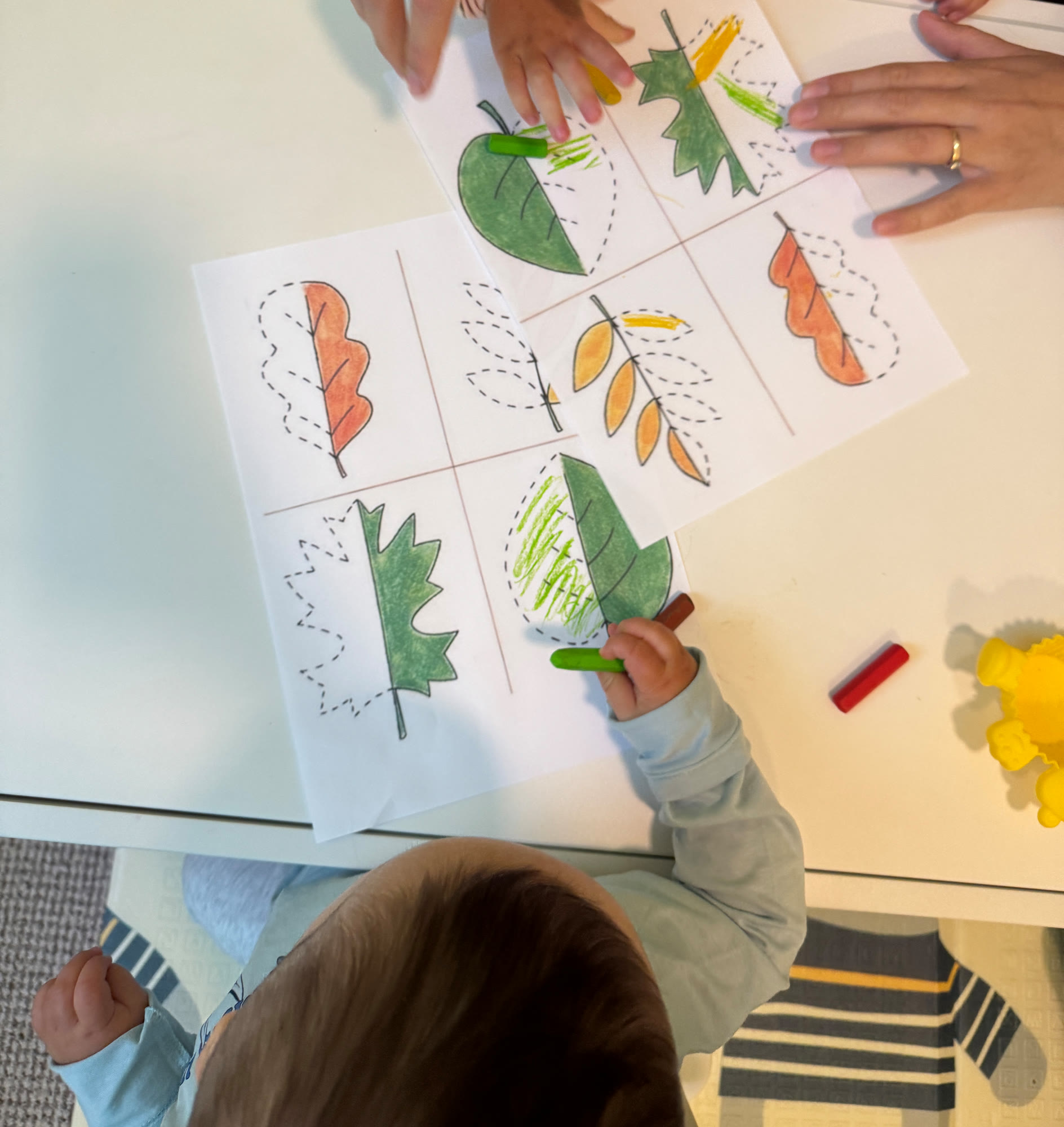 A toddler coloring in autumn leaves at a table, seen from above